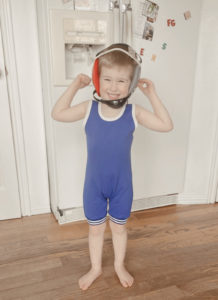 A blonde four year old boy poses in a blue wrestling singlet and headgear