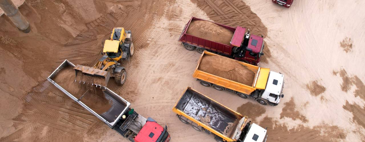 A wheel loader unloads dirt into the back of a dump truck, which is surrounded by other vehicles on a mining site.
