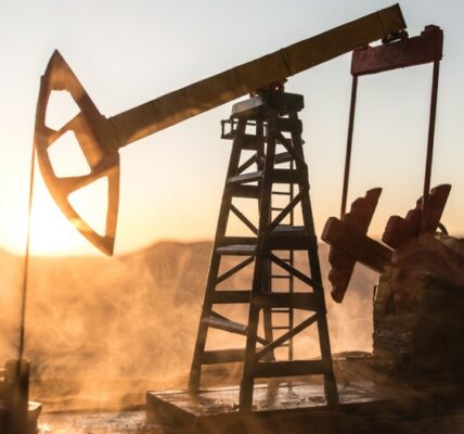 An oil pump at work against the setting sun. Dust is swirling up from the worksite, illuminated in the golden light.