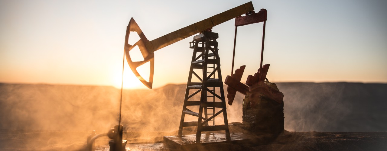 An oil pump at work against the setting sun. Dust is swirling up from the worksite, illuminated in the golden light.