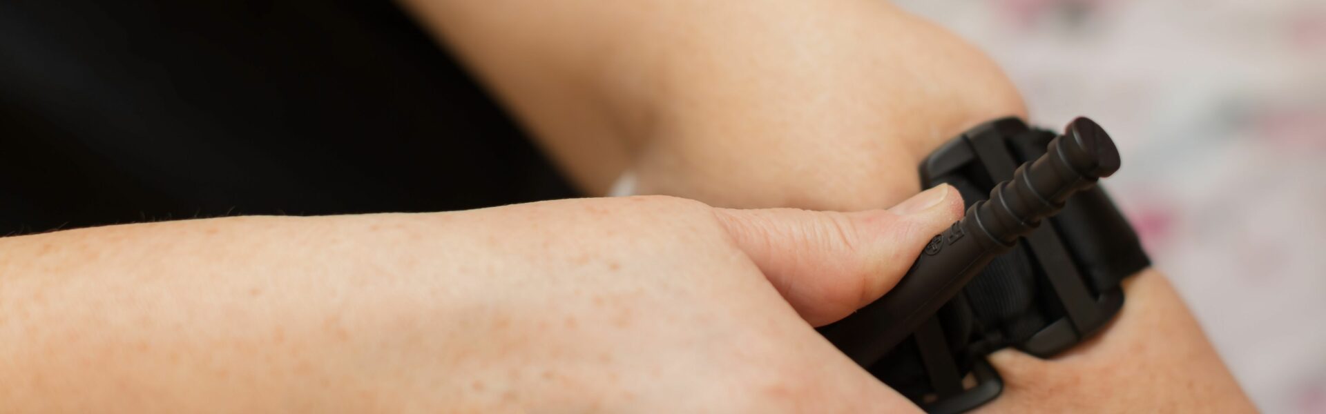 A person applying a self-tightening tourniquet to their arm. They are currently tightening it with their other hand.