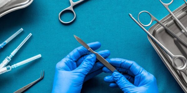 Doctor's hands holding a scalpel over a blue background with various surgical tools laid out on a table.