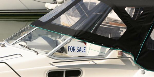 For Sale sign on a cruiser boat featuring a white background with bold, blue lettering indicating the boat is for sale.