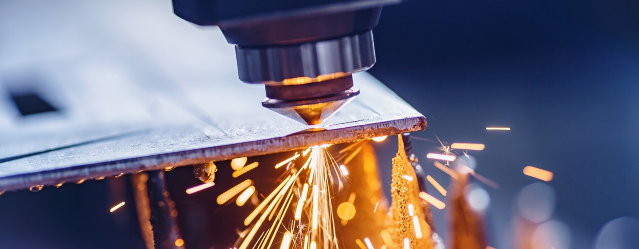 A CNC laser machine cutting a steel sheet. Orange sparks are flying off from the laser contact point.