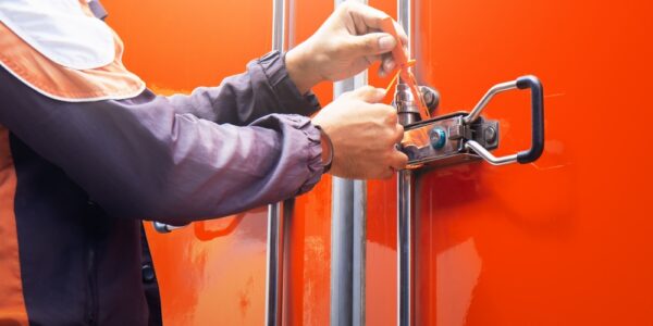 A delivery driver latches a security seal on the backside of a truck with an orange exterior to secure the shipment.