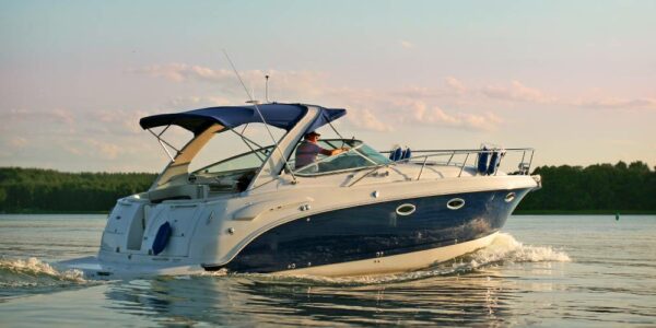 A nice-sized boat cruising on the lake at sunset. The sky is turning pink and orange and the boat is traveling slow.