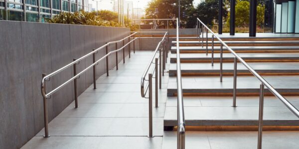 A set of stairs and a ramp leading up to the main entrance of a building. There are two railings close together on the stairs.