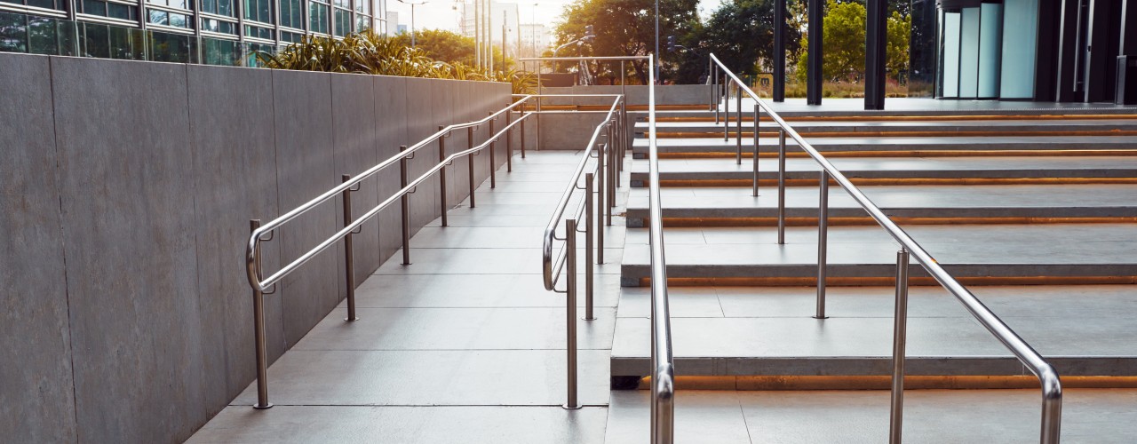 A set of stairs and a ramp leading up to the main entrance of a building. There are two railings close together on the stairs.