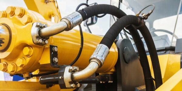 A close-up of a hydraulic system. The equipment is yellow, and two hoses are attached to the machine.