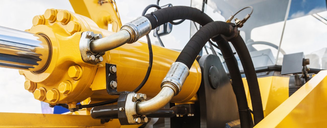 A close-up of a hydraulic system. The equipment is yellow, and two hoses are attached to the machine.