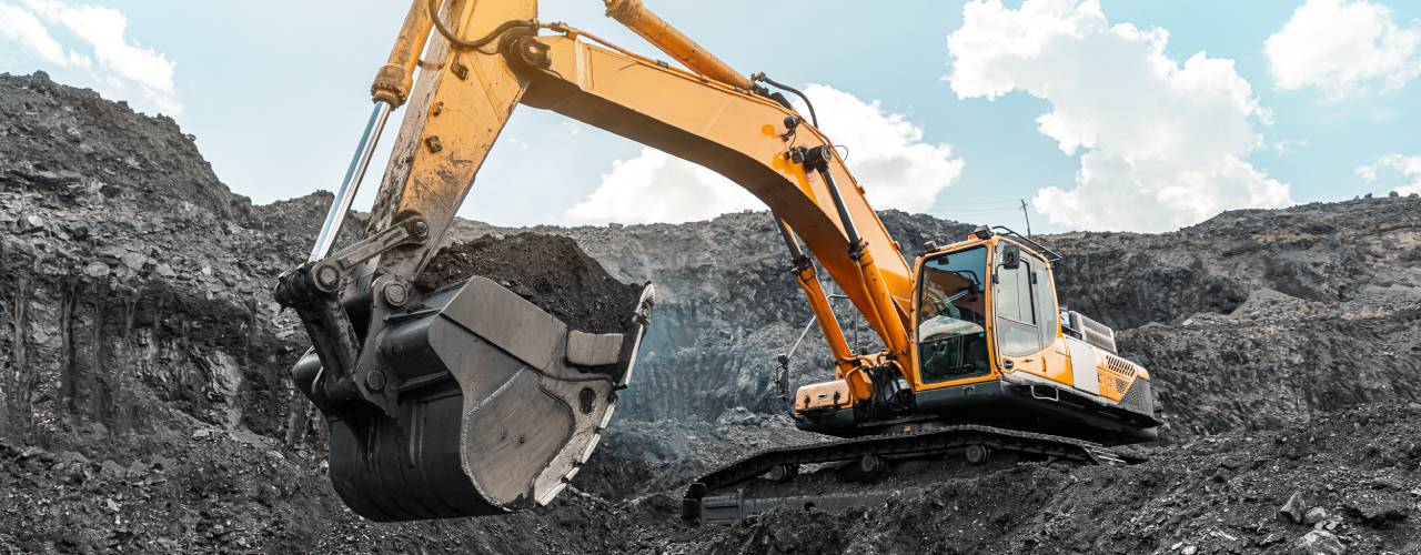 A large excavator stands on the top of a hill at a mining quarry. It carries coal and other minerals in its large bucket.