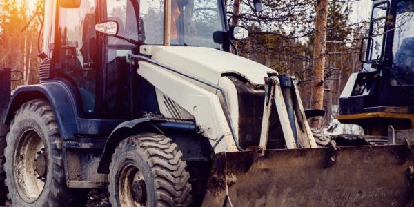 A skid steer loader is parked on muddy ground next to other heavy machinery during a brush clearing project.