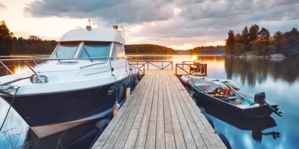 A wooden dock with a boat tied up on either side. The water is calm with the sun setting in the background.