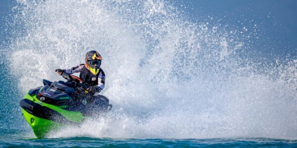 An individual in a helmet and goggles making a big splash in the water while driving a black and green jet ski.