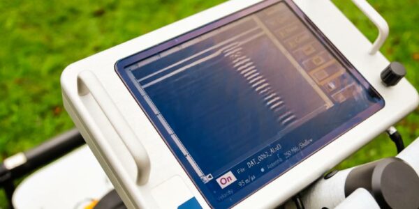 A point-of-view of an operator examining the interface screen of a ground-penetrating radar machine on a grass field.