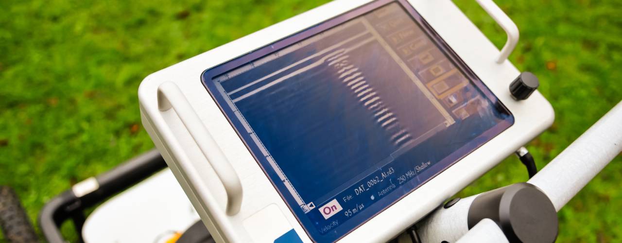 A point-of-view of an operator examining the interface screen of a ground-penetrating radar machine on a grass field.
