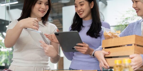 Three young, diverse women are laughing and talking while standing over a donation table with various donated items.