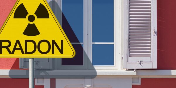 The exterior of a home with coral paint, windows, and shutters, with a large triangular yellow sign that says "RADON."