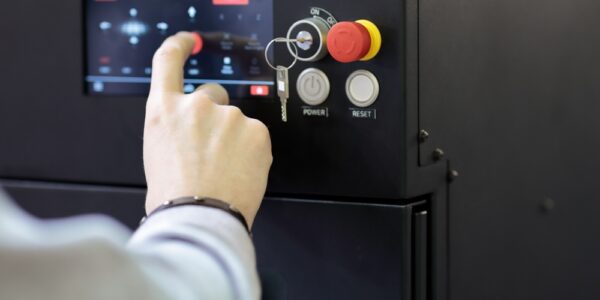 A black control panel with a touch screen, key slot, and red shut-down button. A hand is operating the program on the screen.