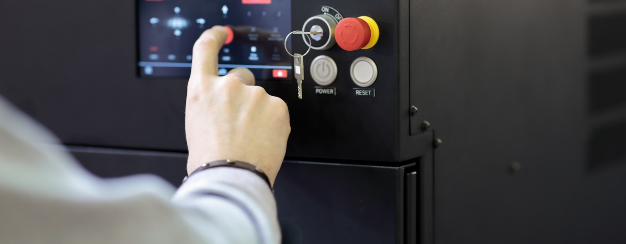 A black control panel with a touch screen, key slot, and red shut-down button. A hand is operating the program on the screen.