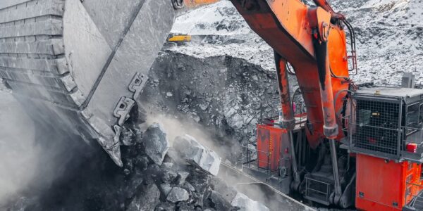 A red excavator dumping coal into the top of a dump truck. There is some snow on the piles of rocks in the background.