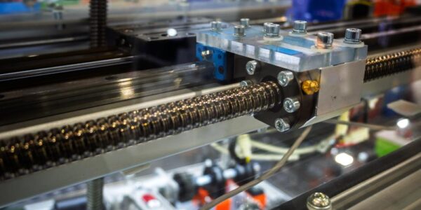 Close-up of the linear ball screw of an automated metal machine with multiple cables and attachments.