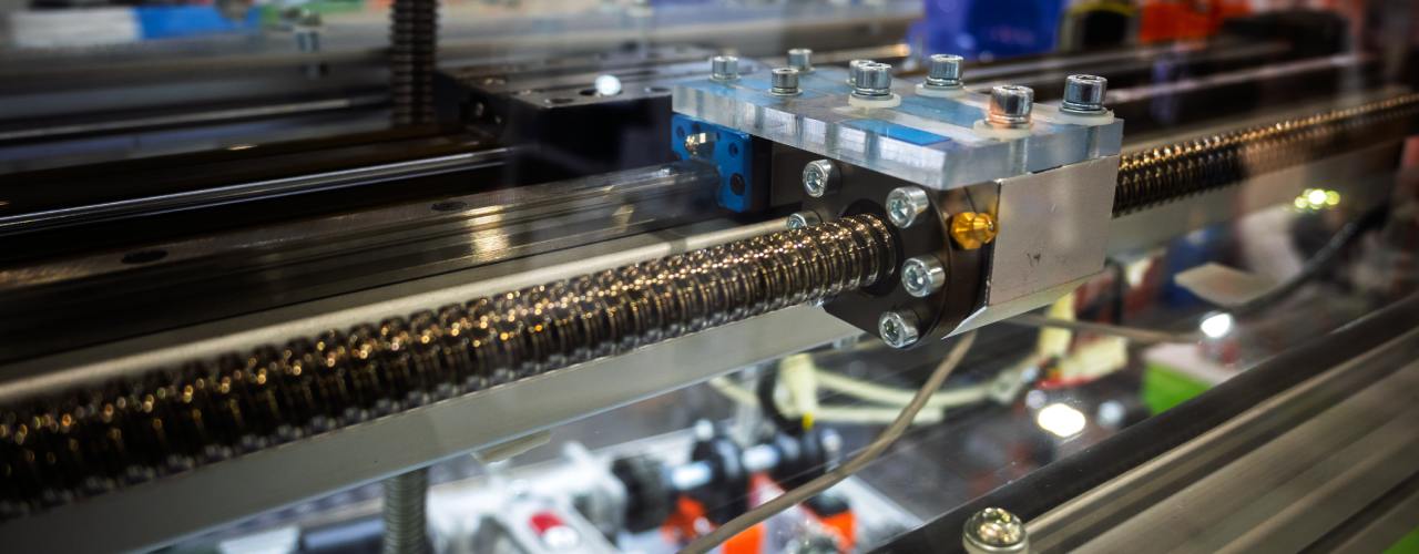 Close-up of the linear ball screw of an automated metal machine with multiple cables and attachments.