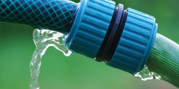 A close-up of a hose's blue twisting cap connecting two hoses, with a leak springing from one side.