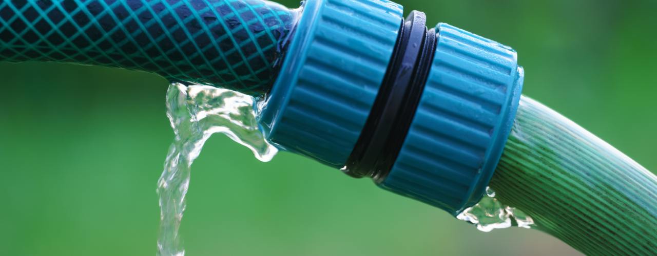 A close-up of a hose's blue twisting cap connecting two hoses, with a leak springing from one side.
