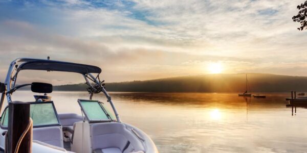 A boat with a white interior is moored to a wooden dock on a misty lake with the sun rising in the distance.