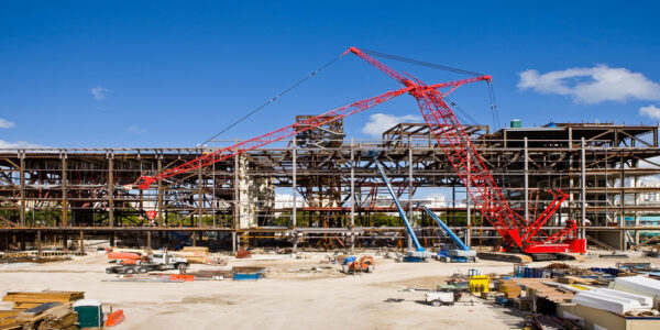 A multi-story building mid-construction with exposed interiors and construction equipment all around the structure.