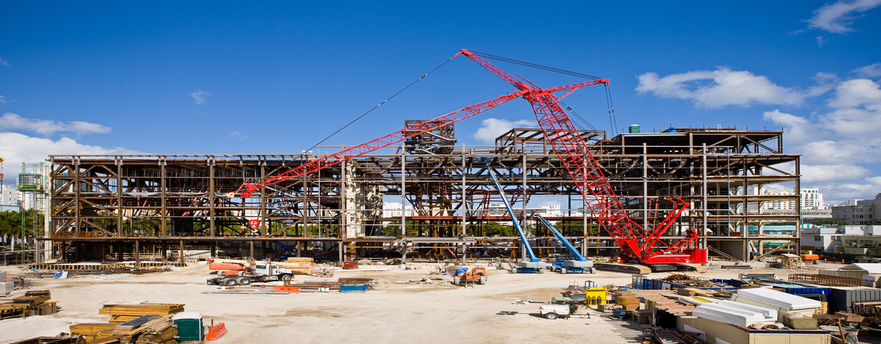A multi-story building mid-construction with exposed interiors and construction equipment all around the structure.