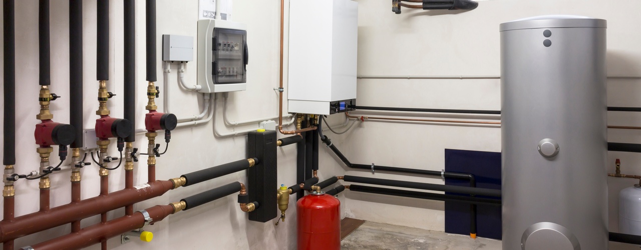 A boiler room area in an unfinished basement with a solar tank and exposed pipes along the wall and ceiling.