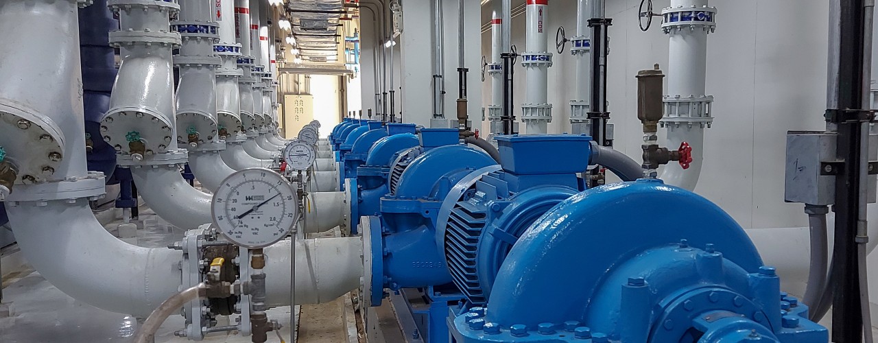 Several electric motors mounted on metal frames and connected to water pumps with piping in an industrial mechanical room.
