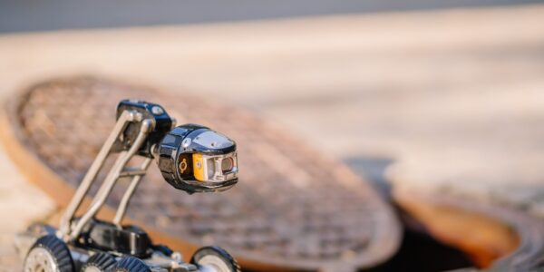 A small, robotic camera on six wheels on a bricked surface next to a manhole sewer opening with the lid partially off.
