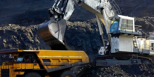 An operator in a white excavator loads up coal into a yellow bedding box as it works on a coal mining job site.