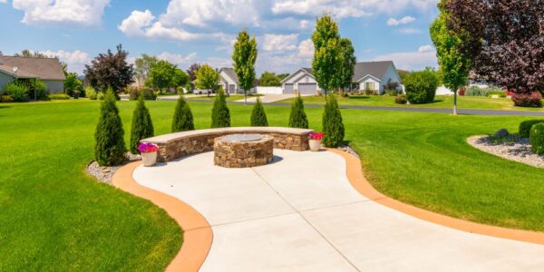 A backyard with a functional firepit in the center of a paved walkway. The bench seating is surrounded by mini trees.