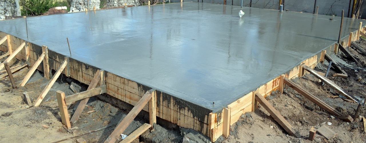 A freshly-poured foundation for a home with timber formwork and metal reinforcement on a construction site.