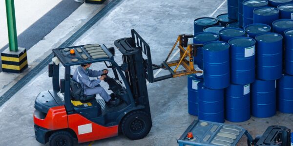 A loading area with several blue drums stacked on top of each other. Someone driving a forklift moves the drums.