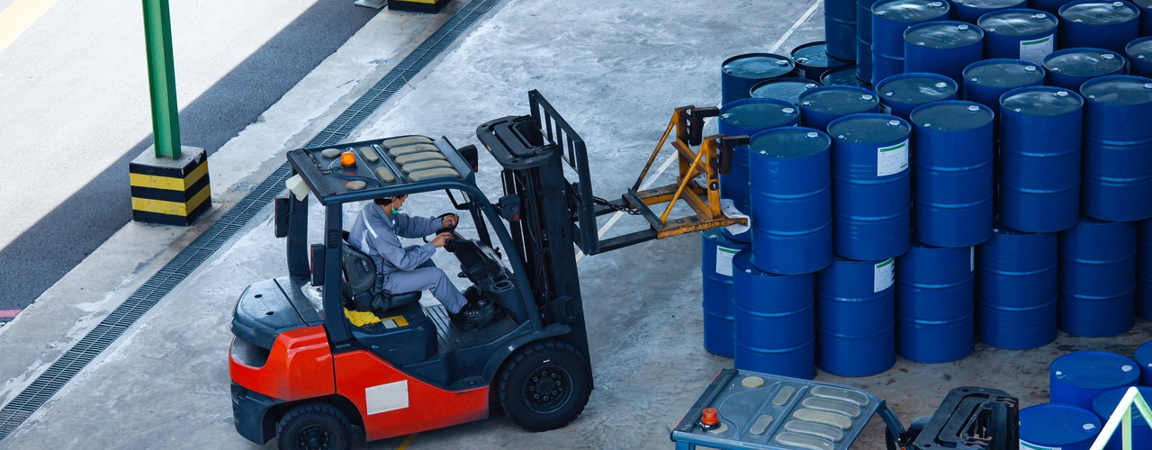 A loading area with several blue drums stacked on top of each other. Someone driving a forklift moves the drums.