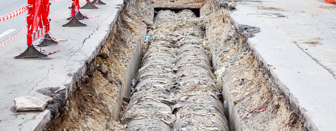 A section of road with an excavation site. There are two underground pipelines stretching underneath an urban street.