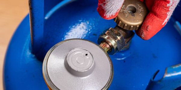 A close-up view shows a person wearing a work glove turning the bronze valve on a blue gas cylinder.