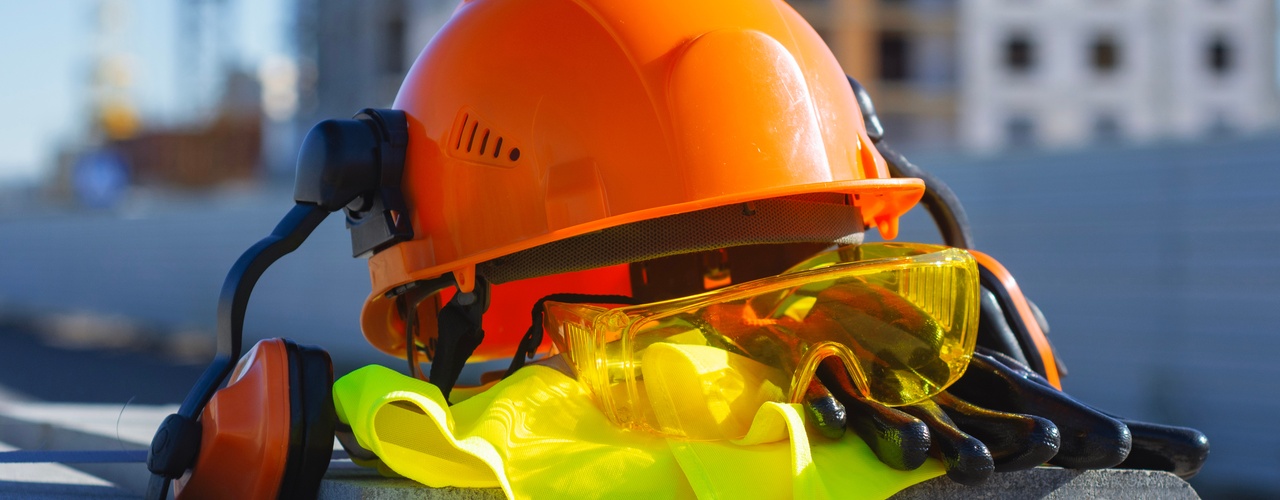 Construction PPE piled on top of each other. There is an orange hard hat, safety glasses, a vest, and gloves.