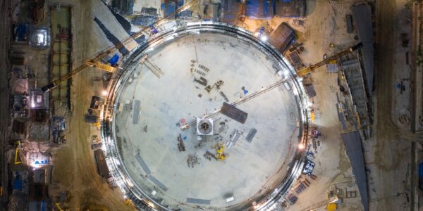 an illuminated industrial construction site at night with cranes, a circular structure, and surrounding work areas.