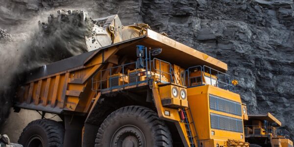 A yellow haul truck is being loaded with dark coal by a large loader beside a layered rock wall in an open mine.