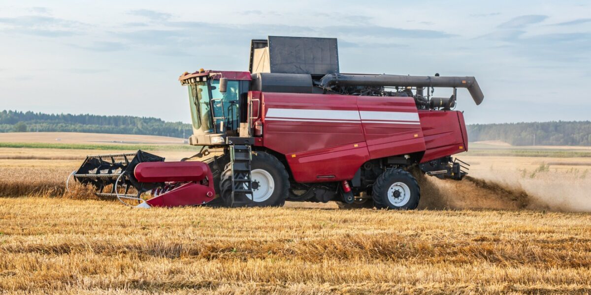 A side view of a red combine harvester harvesting wheat in a large agricultural crop field during the day.