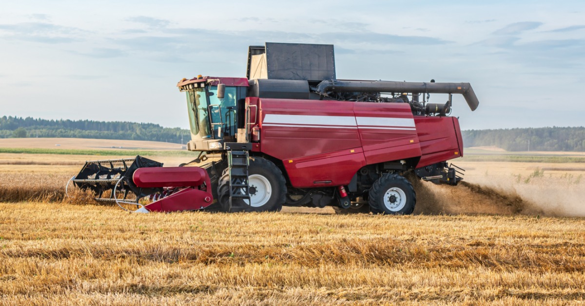 A side view of a red combine harvester harvesting wheat in a large agricultural crop field during the day.