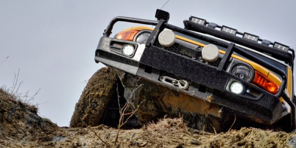 A view of the front part of a Ford Bronco with a large metal protection, driving up a hill covered in mud and rocks.