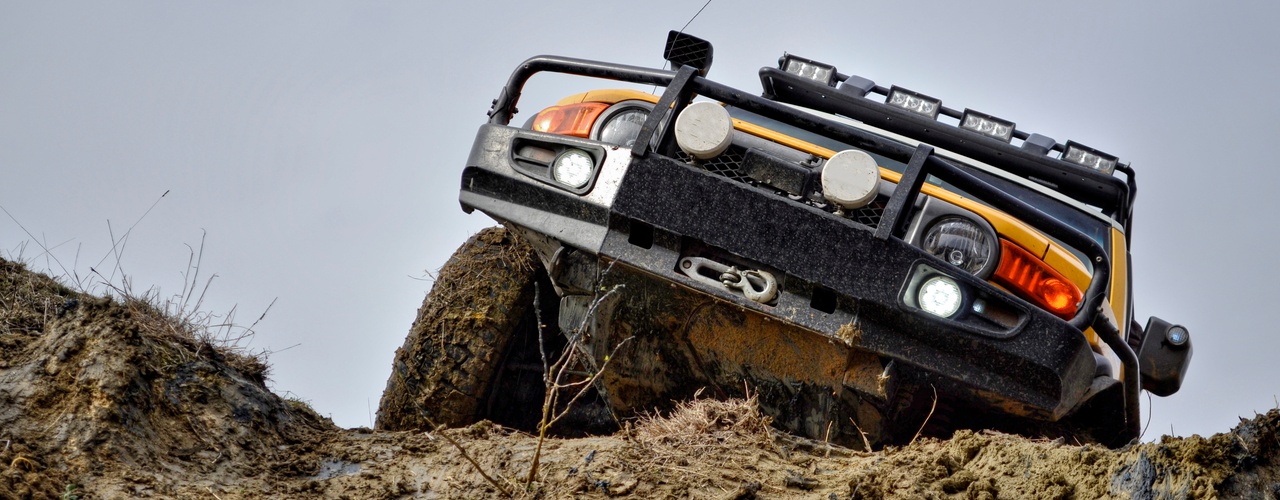 A view of the front part of a Ford Bronco with a large metal protection, driving up a hill covered in mud and rocks.