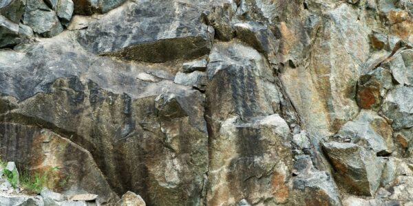 Close-up of a rugged rock face with jagged gray and brown stone formations, deep cracks, and scattered loose rocks.